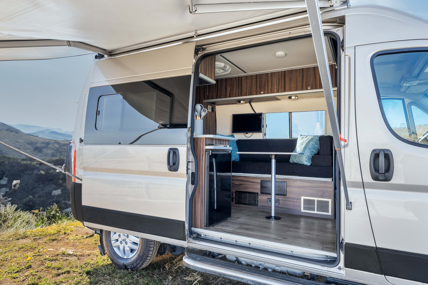 This rv rental reveals its spacious interior with an open door, extended awning, and cozy seating area overlooking mountains.