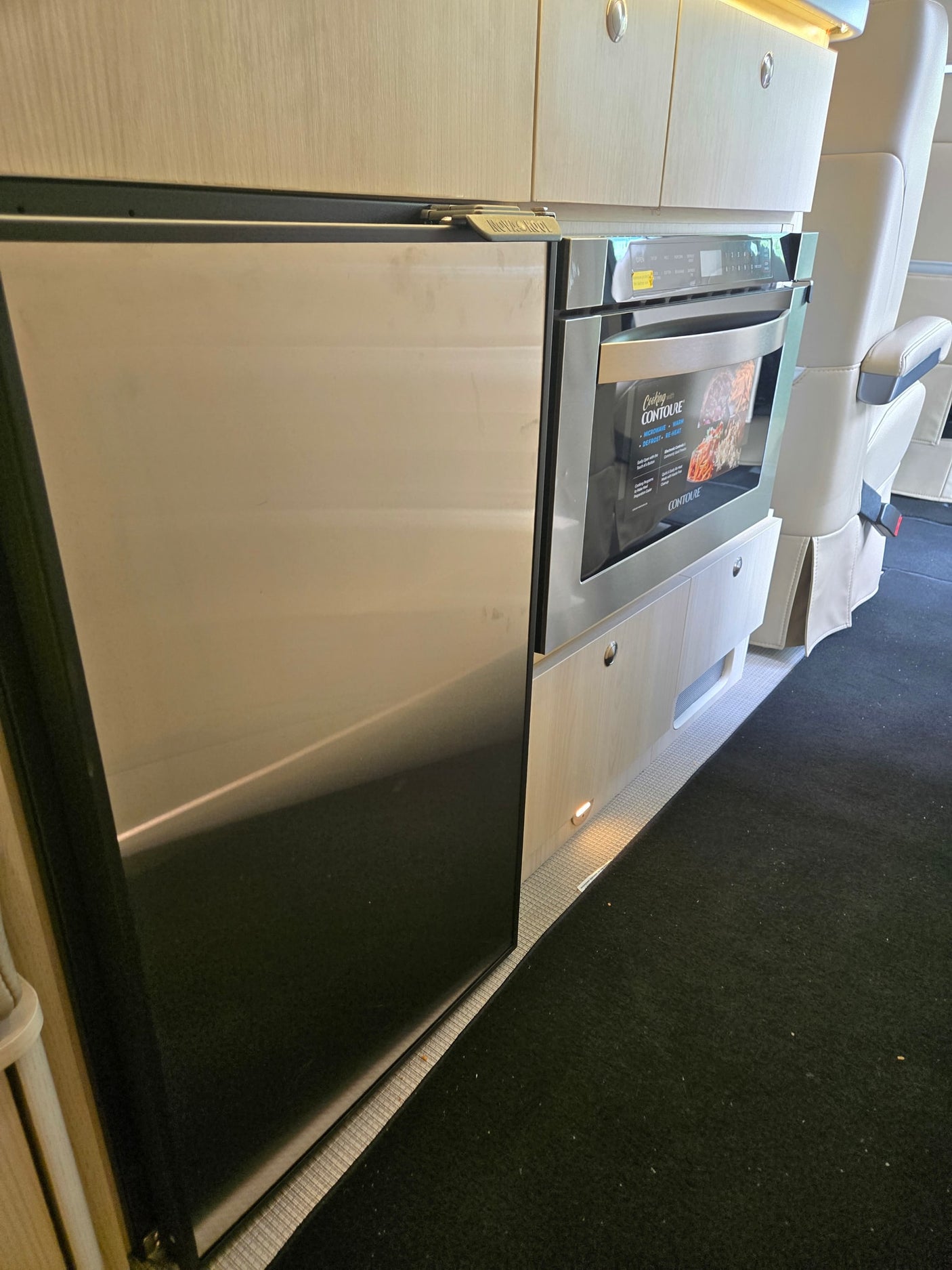 RV rental kitchen: stainless Contoure microwave & fridge, secured with a 'MOVING ON UP' latch, within light wood cabinetry.