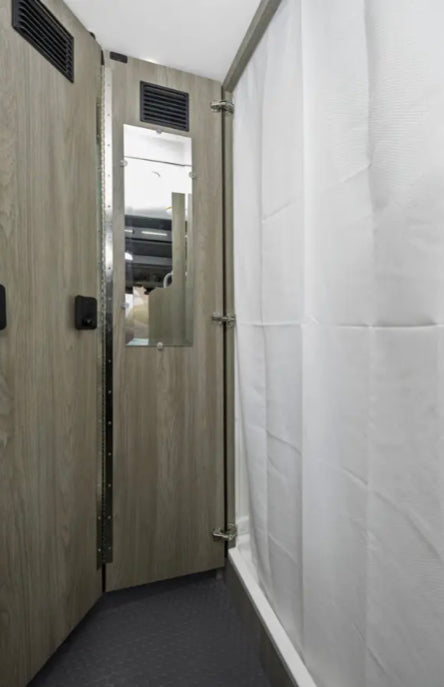 RV rental interior: compact bathroom with a white shower curtain, small mirror, and wood-grain paneling.
