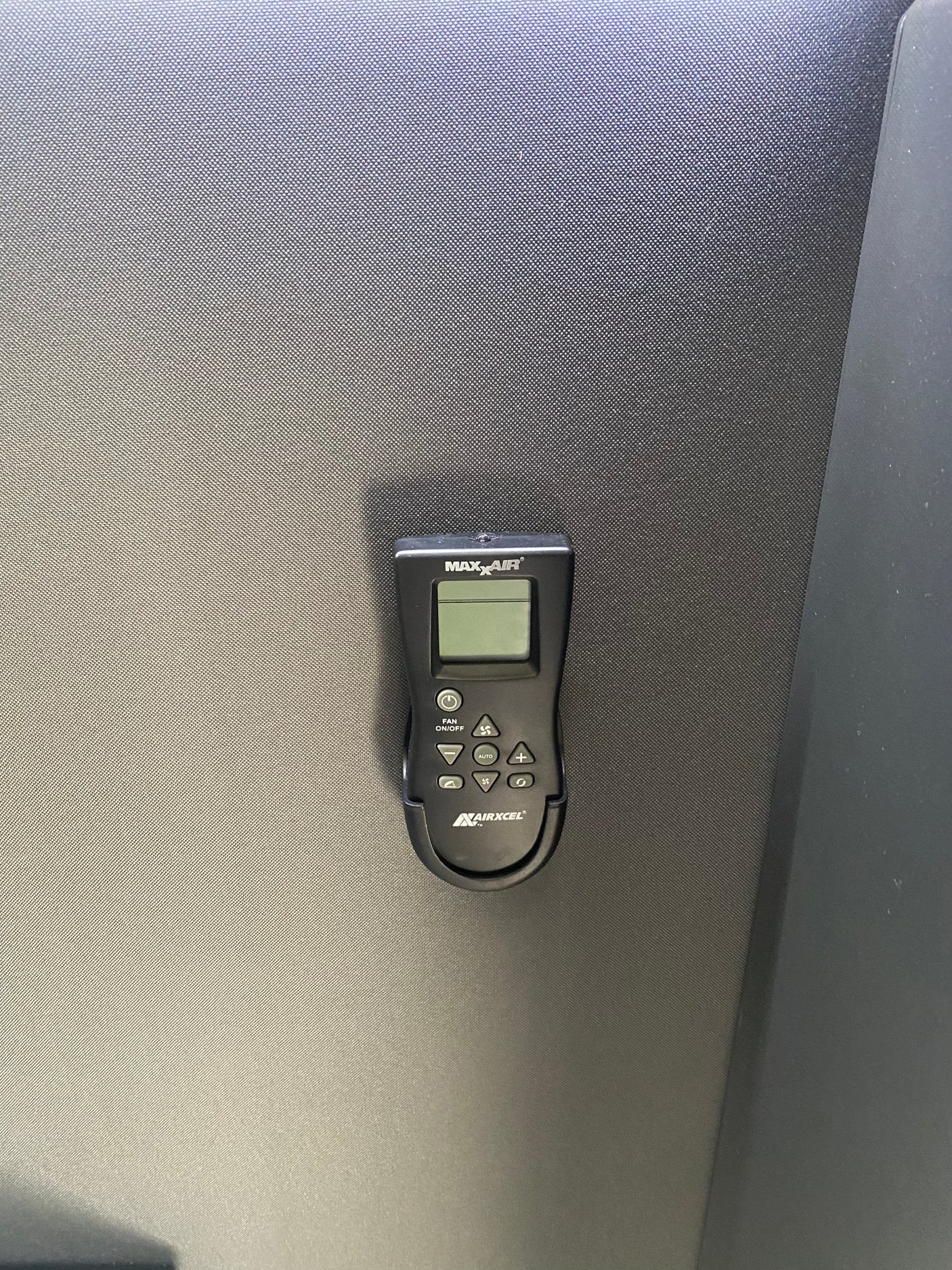 MaxxAir remote control on textured surface, essential for RV rental climate management, with buttons for fan, temp, modes.