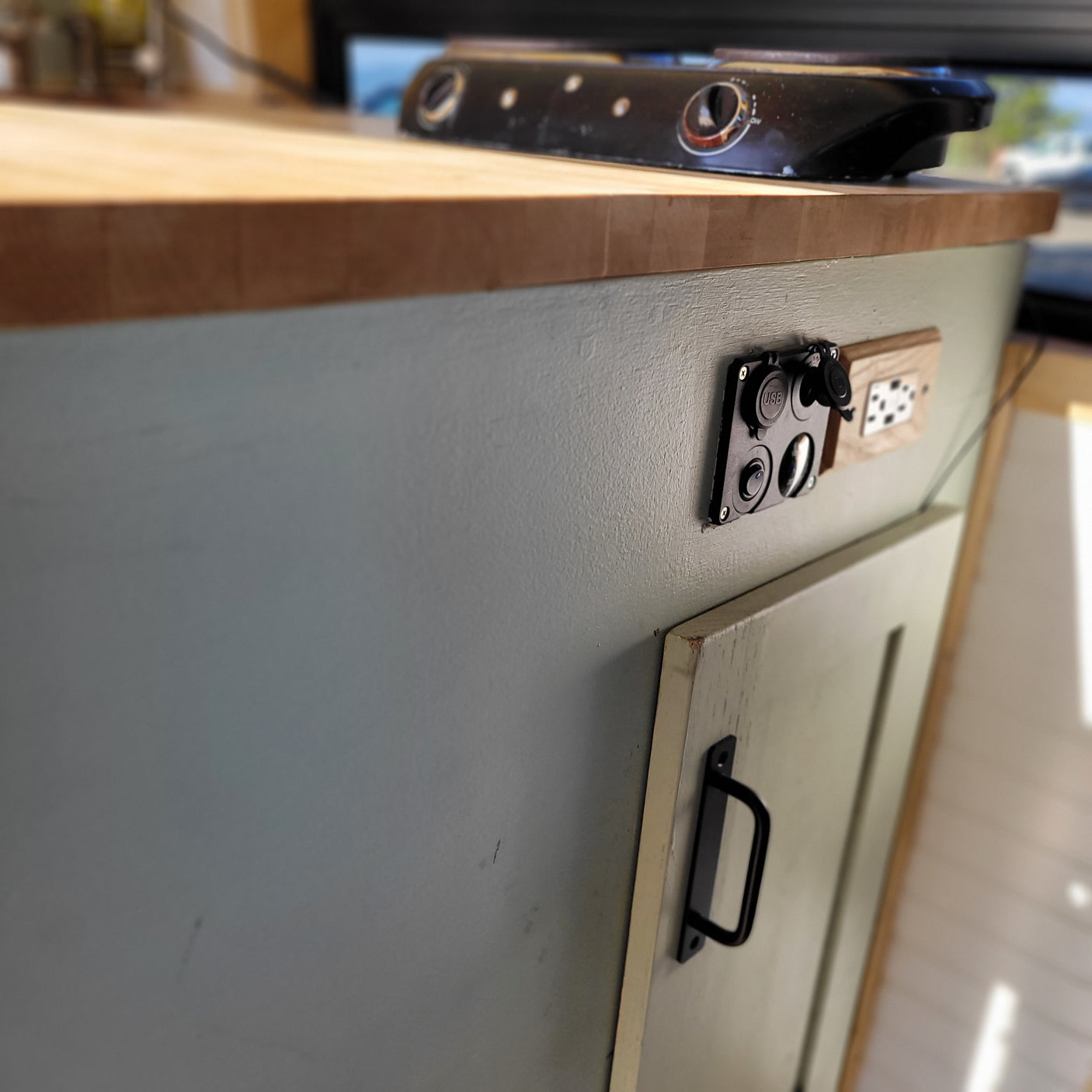 RV rental interior: A wooden counter, portable electric stove, and essential USB/power outlets for convenience.