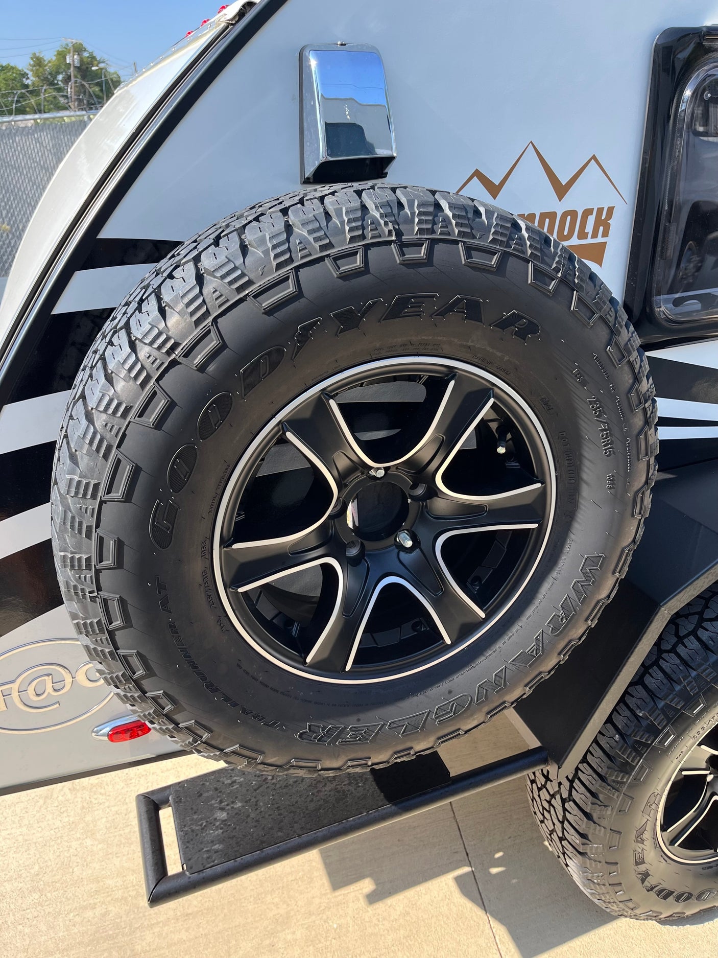 Close-up of an RV rental's rear, showcasing a new Goodyear Wrangler 235/75R15 spare tire on a black wheel.