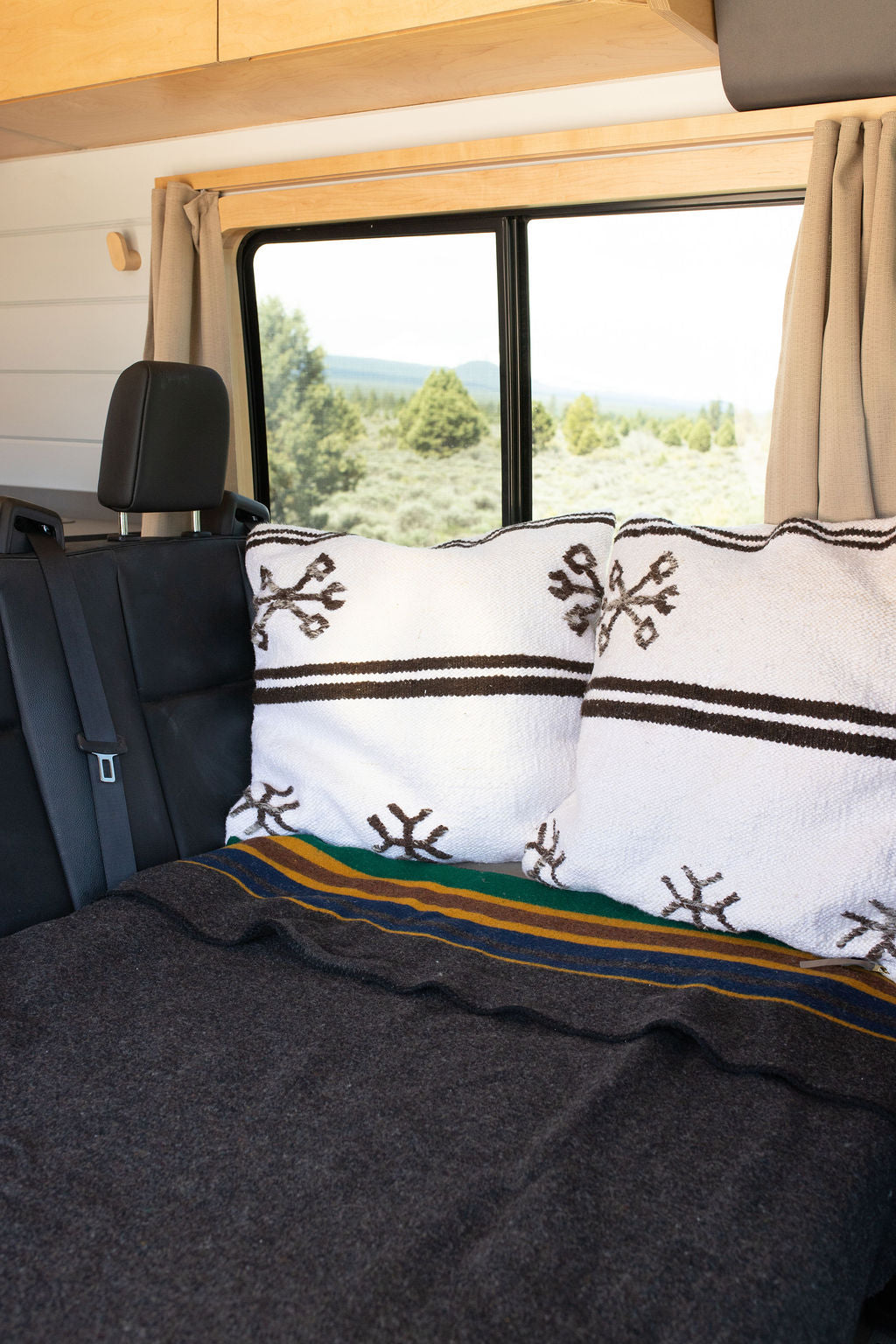 Enjoy comfort on your RV rental journey. Plush pillows & a striped blanket on the back seat, with a scenic nature view.