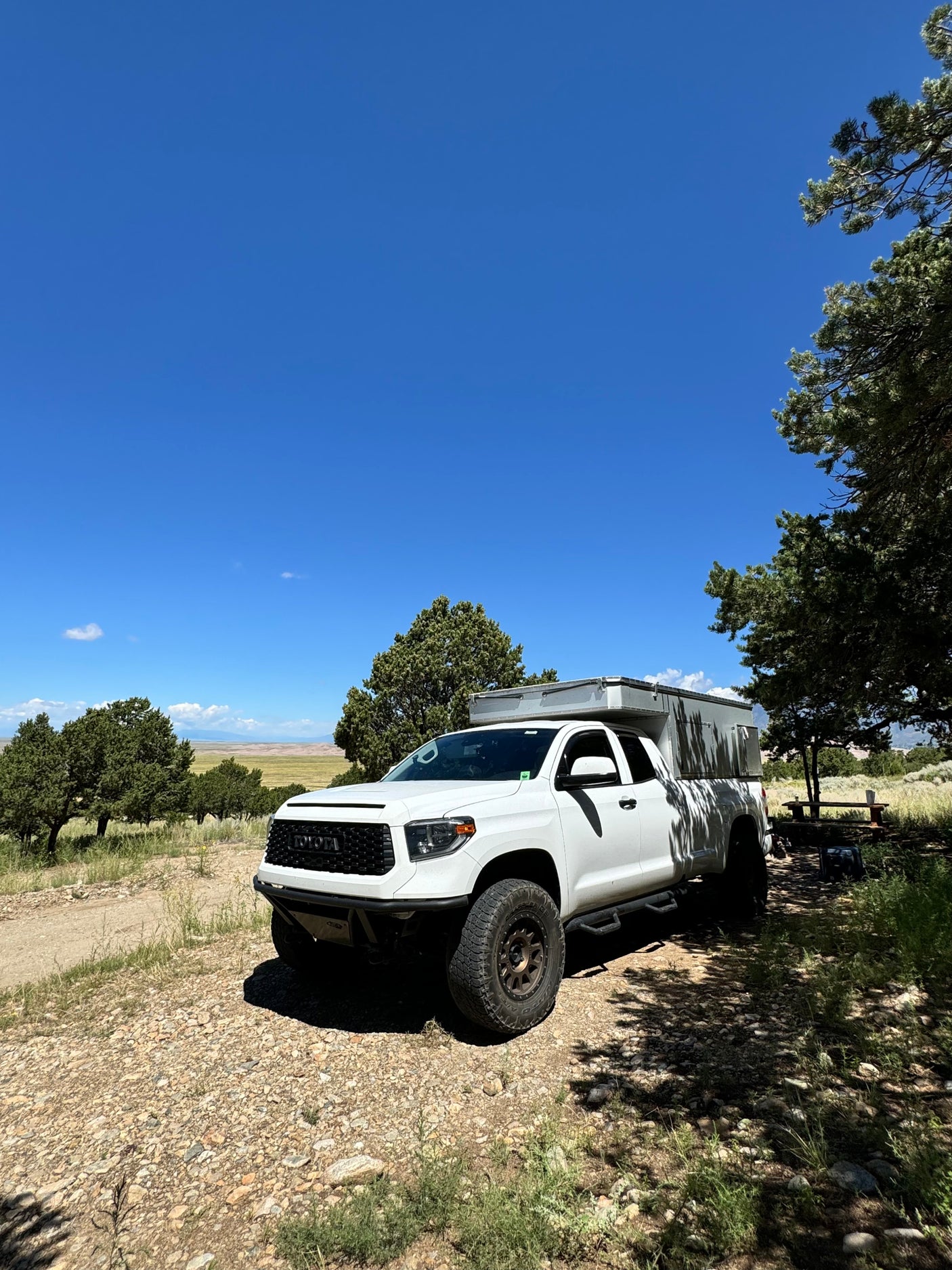White Toyota Tundra truck camper, an RV rental ready for scenic off-road camping adventures under a blue sky.
