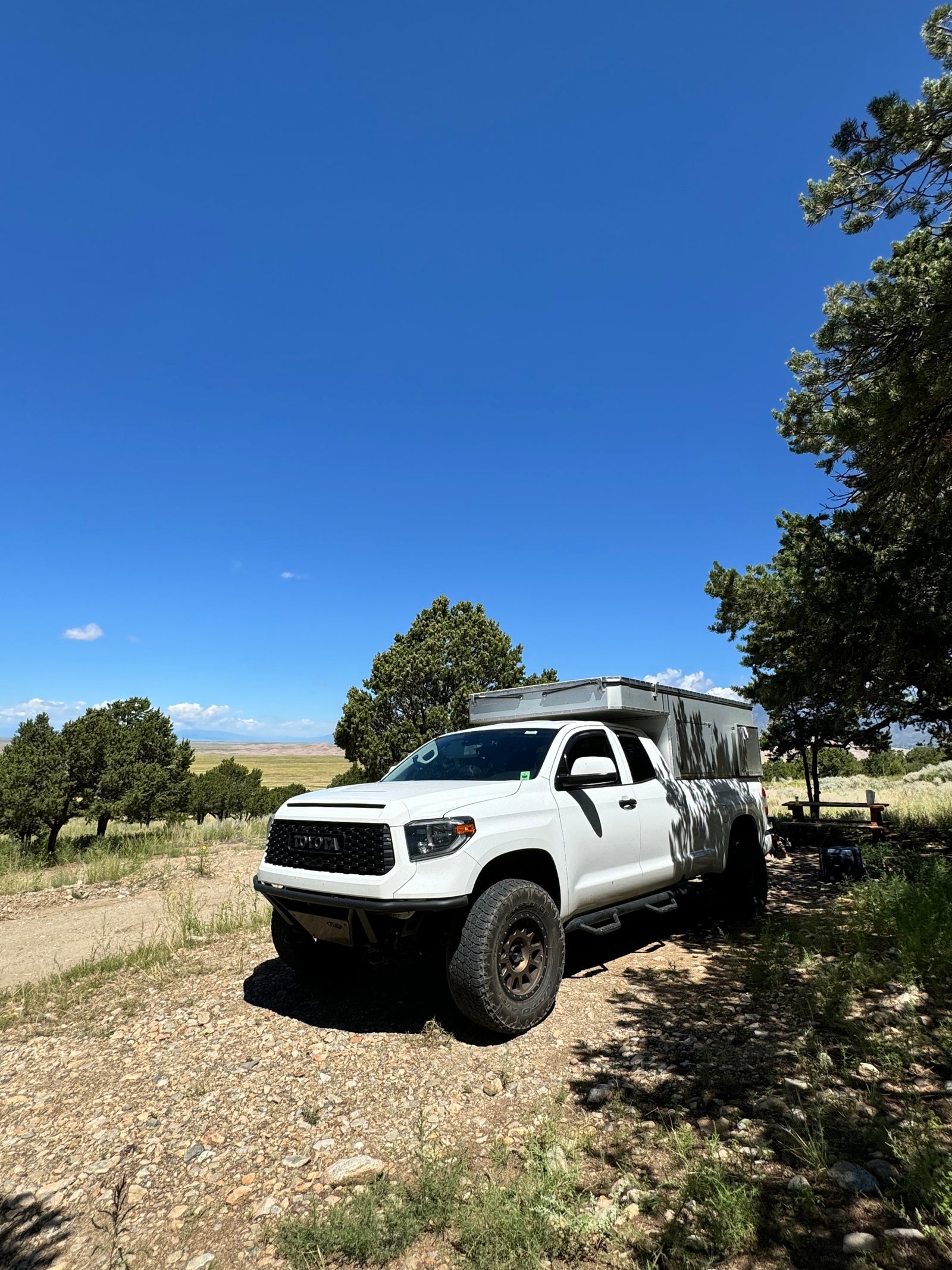 White Toyota Tundra truck camper, an RV rental ready for scenic off-road camping adventures under a blue sky.