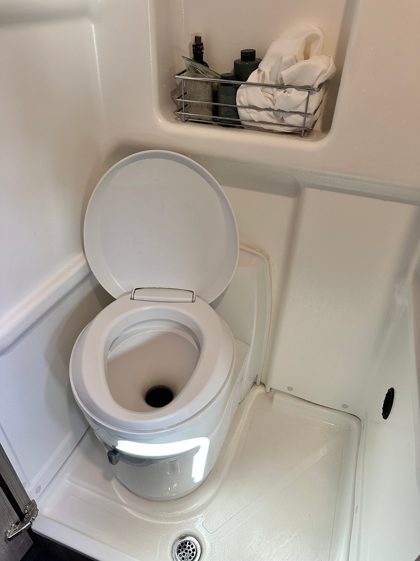 This RV rental bathroom features a compact toilet and a shower stall with a shelf for toiletries.