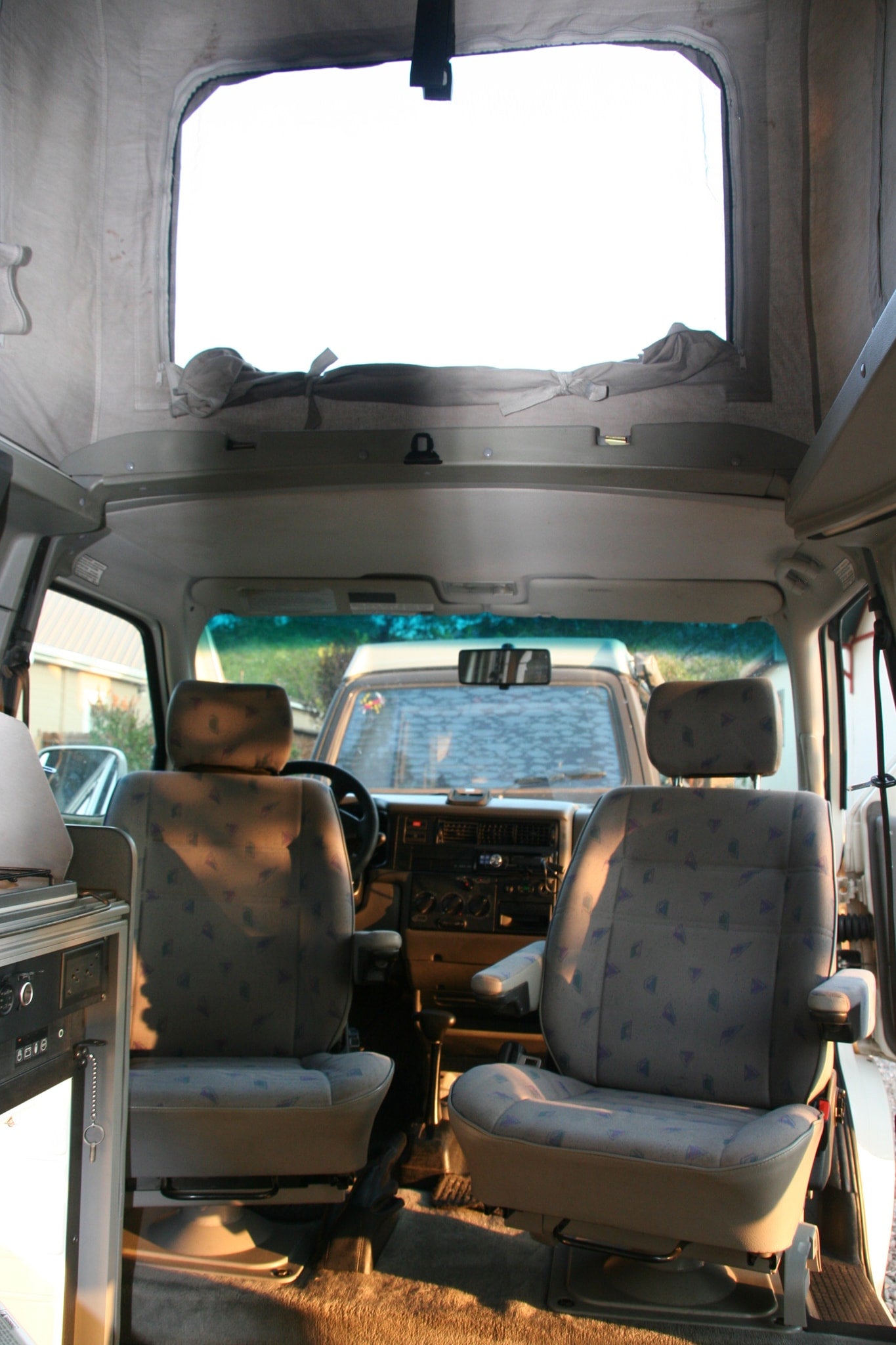 RV rental interior: front seats, dashboard, and second-row seats with a bright side window and tie-back curtains.
