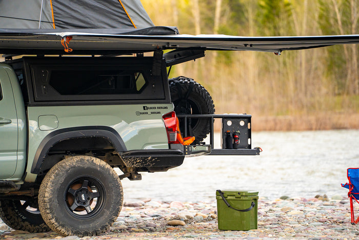 a great alternative to an rv rental.|Sage green overlanding truck with rooftop tent & awning on riverbank. Great for an RV rental outdoor adventure.|Green Yeti cooler on river rocks with an overland truck and awning
