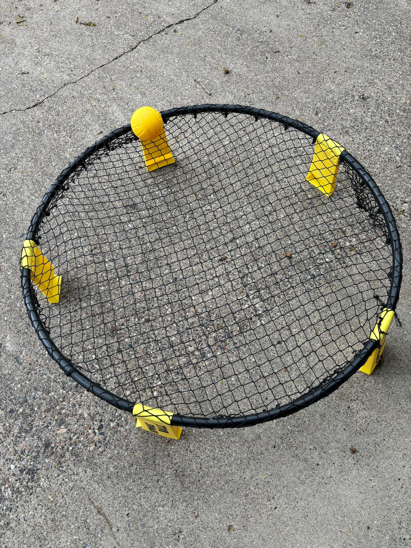 Spikeball set with black net, yellow ball and feet on concrete. Great for outdoor fun on your RV rental trip!