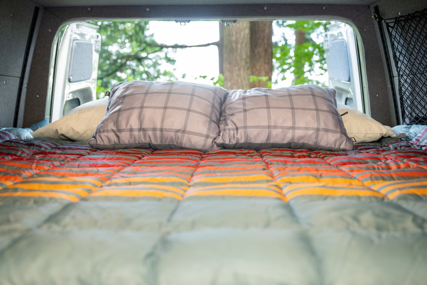 Cozy RV rental bed with open back doors revealing a natural view. Perfect for van life adventures from inside a campervan.