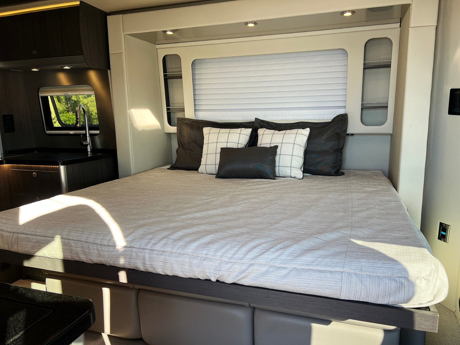Relax in this comfortable RV rental, featuring a cozy bed, modern compact kitchen with a sink, and window views.