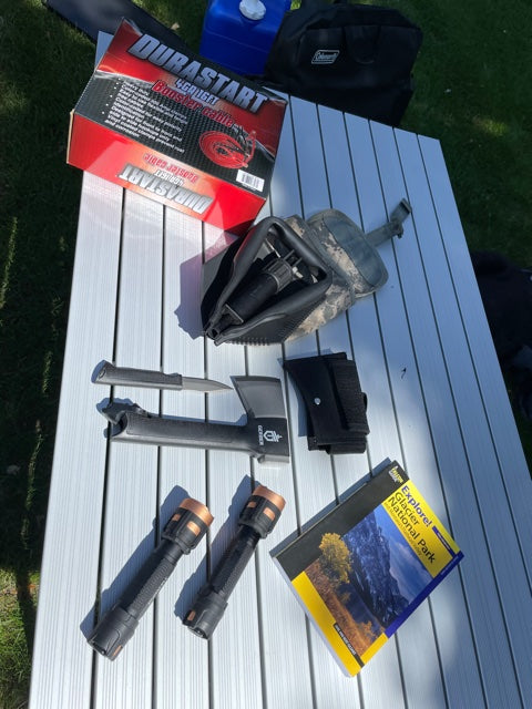 RV rental trip essentials: Durable tools, bright flashlights, booster cables, and a park map on a camping table.