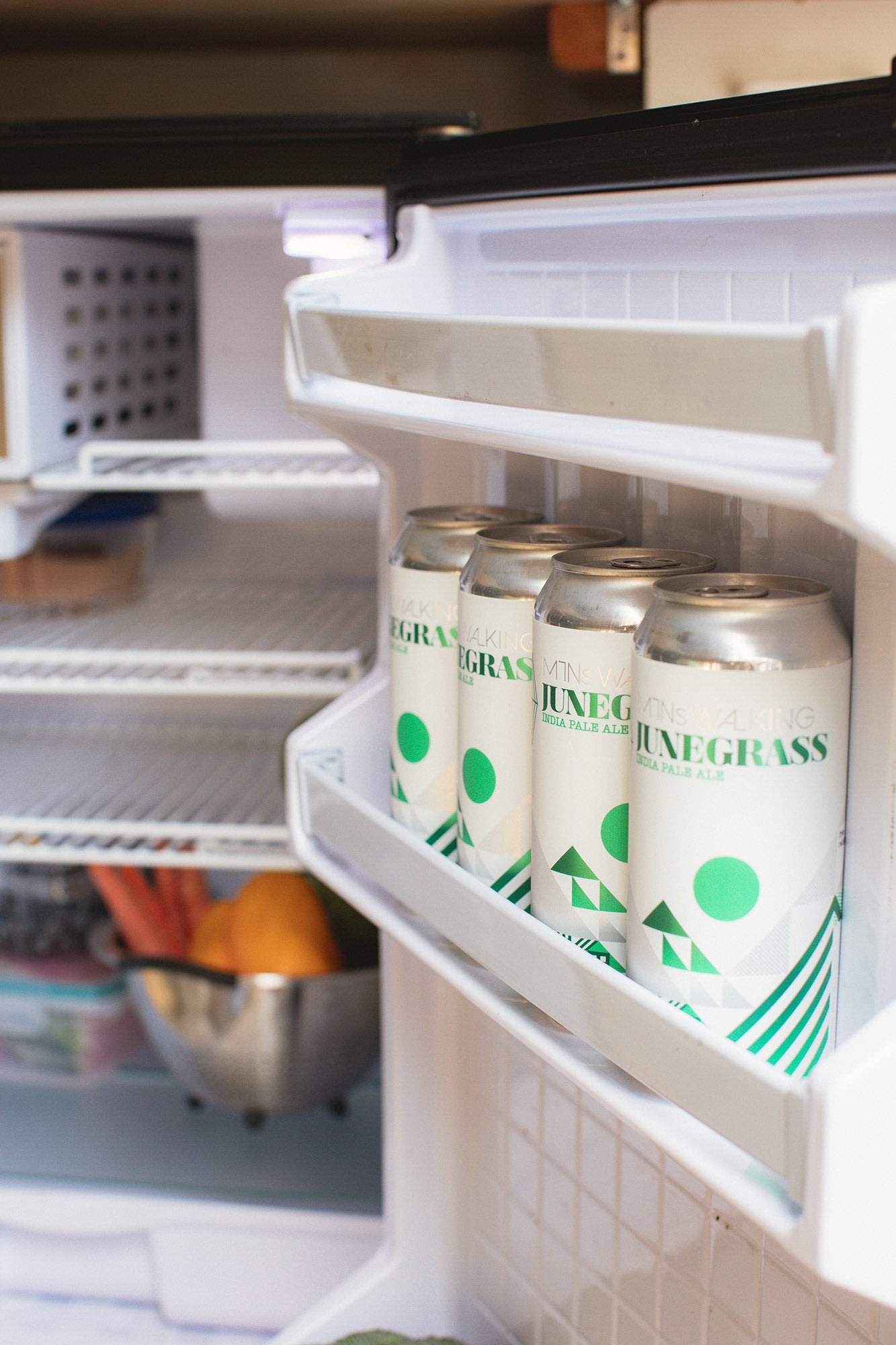 An open fridge in an RV rental, stocked with Junegrass IPA cans and fresh veggies for your adventure.