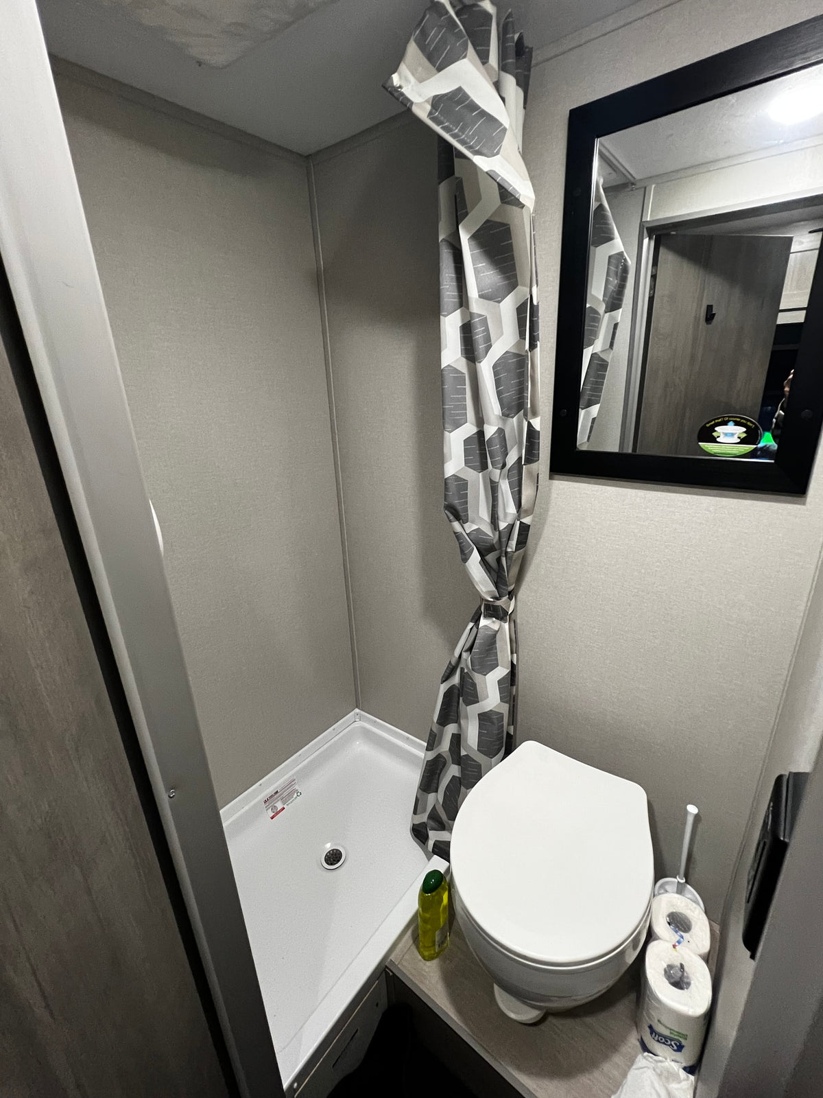 Compact RV rental bathroom: a functional space featuring a shower with a patterned curtain, toilet, and mirror. — photo 10
