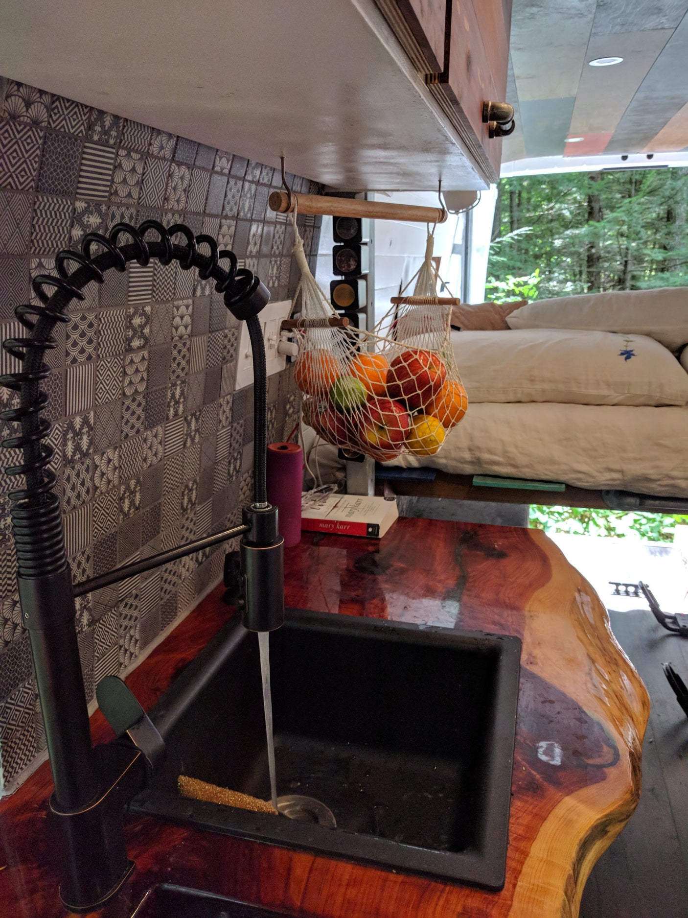 Stylish RV rental kitchen with a black faucet, running water in the sink, live-edge wooden counter, and a hanging fruit net.