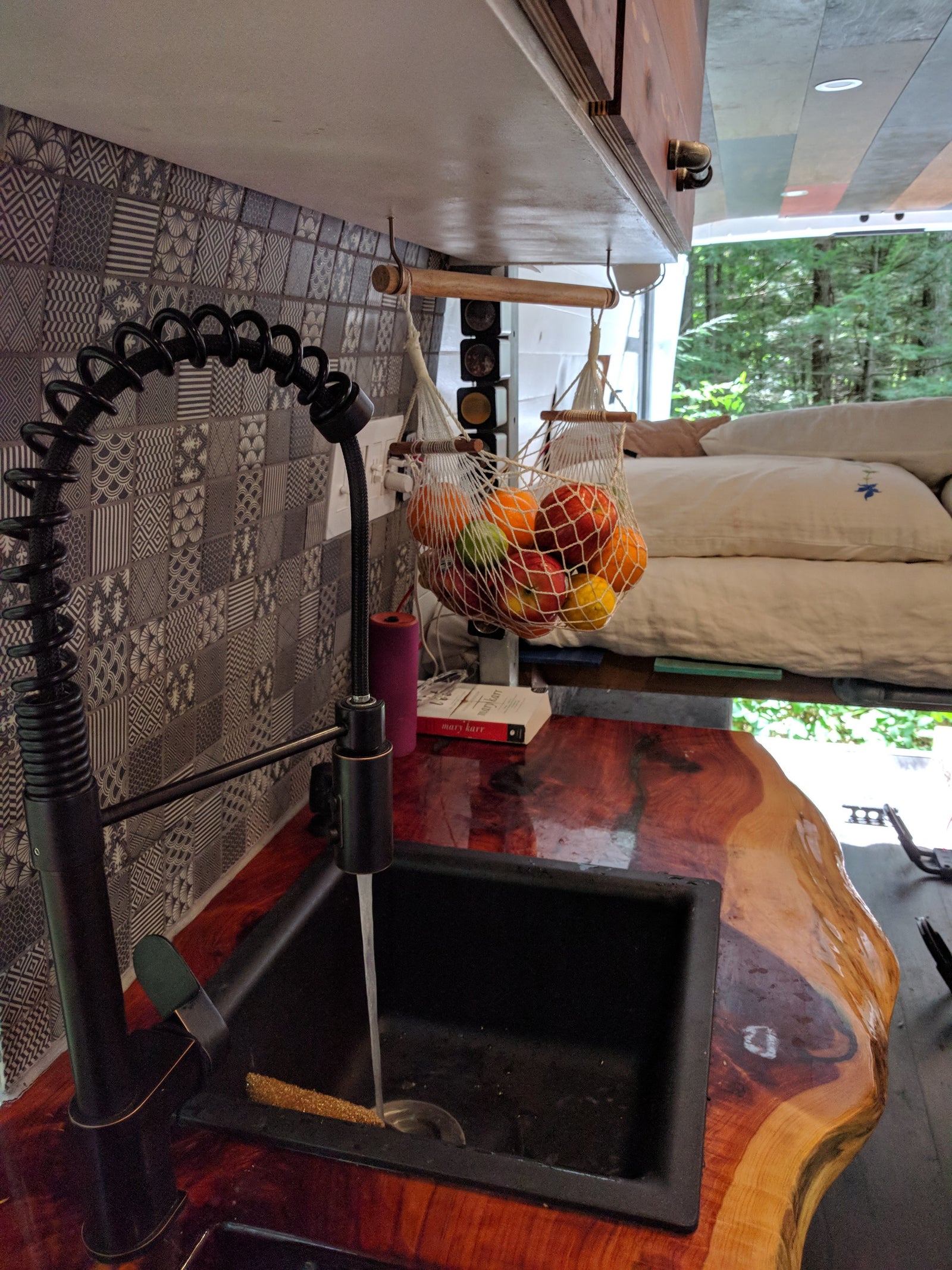 Stylish RV rental kitchen with a black faucet, running water in the sink, live-edge wooden counter, and a hanging fruit net.