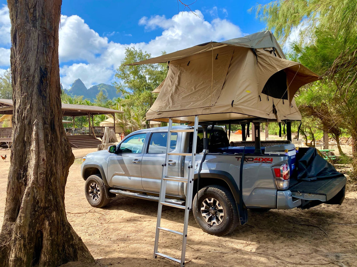 Grey Tacoma pickup with a large rooftop tent & ladder in a scenic outdoor setting, ideal for an rv rental adventure.