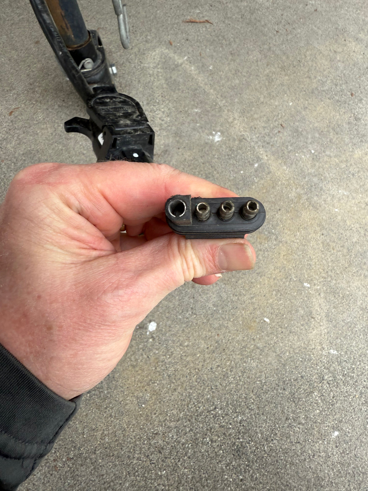 A hand holds a black 4-pin trailer connector (one large, three small holes), vital for RV rental lighting. Hitch in background. — photo 13