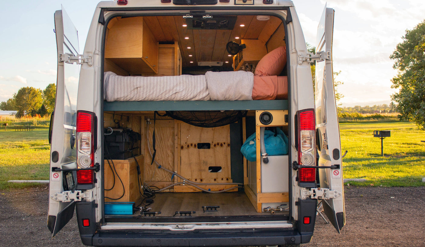 Custom camper van, perfect for an RV rental adventure, reveals its cozy bed, ample storage, and utility setup through open rear doors.