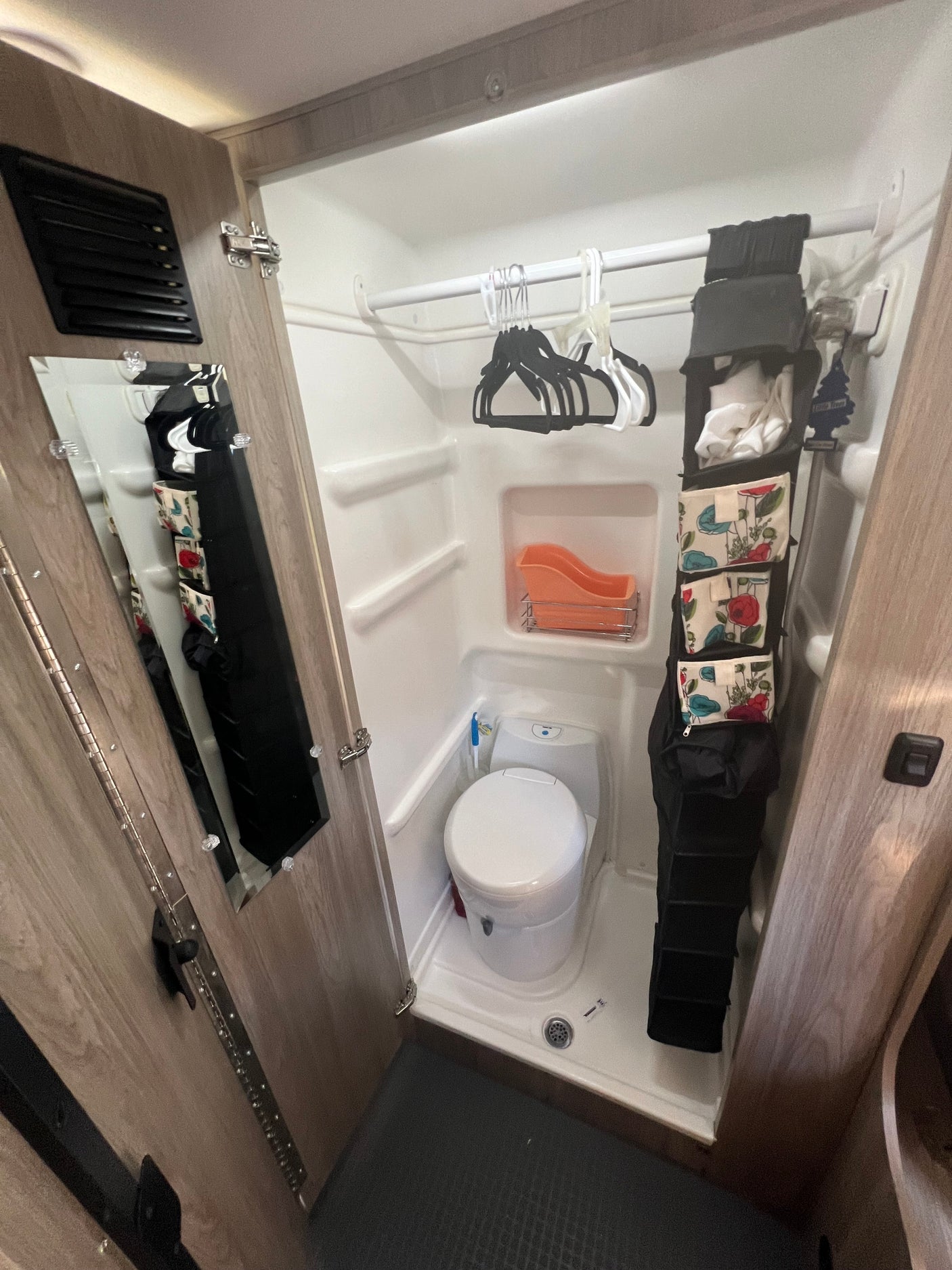 Inside an RV rental: a compact wet bath with toilet, shower, hanging storage, and door-mounted mirror.