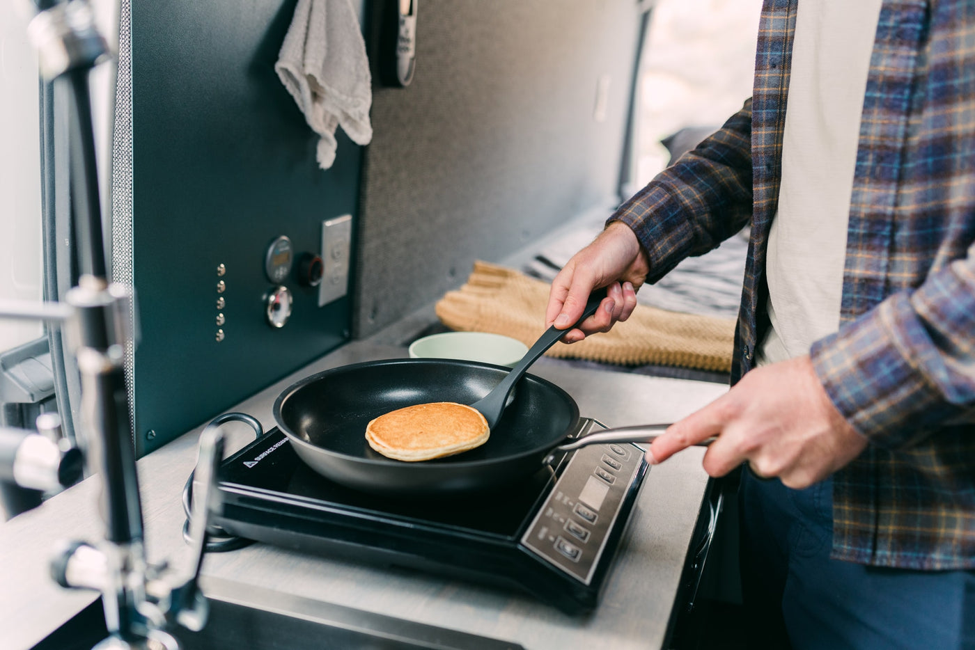 Making breakfast in an RV rental: a person flips a pancake on a portable stove in a cozy camper kitchen. — photo 19