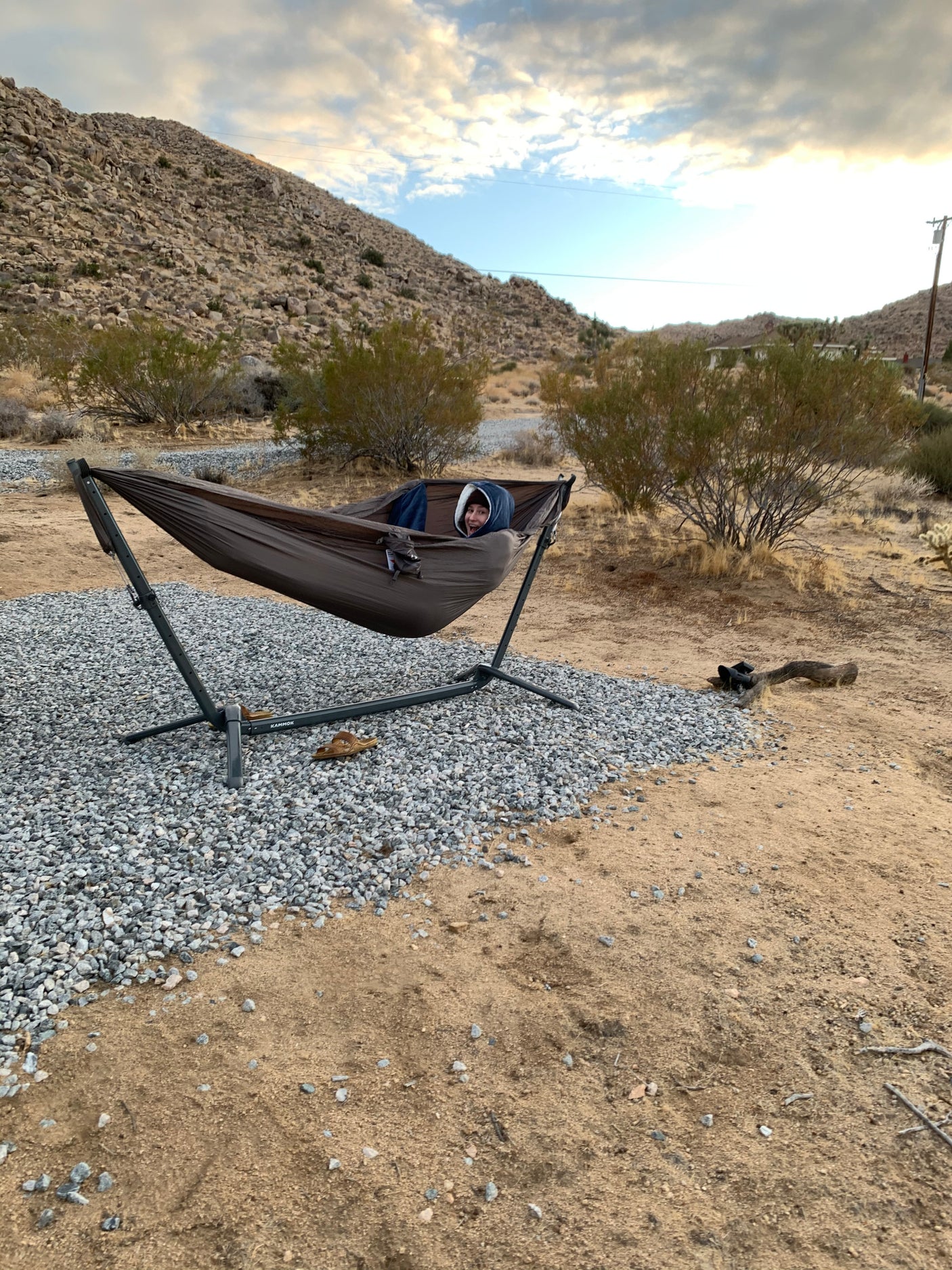 Relaxing in a desert hammock, a person smiles from their stand on gravel. An RV rental allows for such serene escapes.