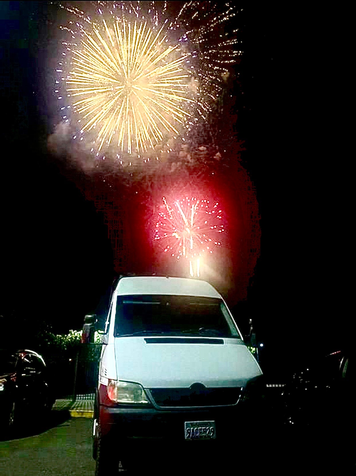 Fireworks illuminate a parked **rv rental** van at night. Golden and red bursts explode above the vehicle, offering a vibrant view.