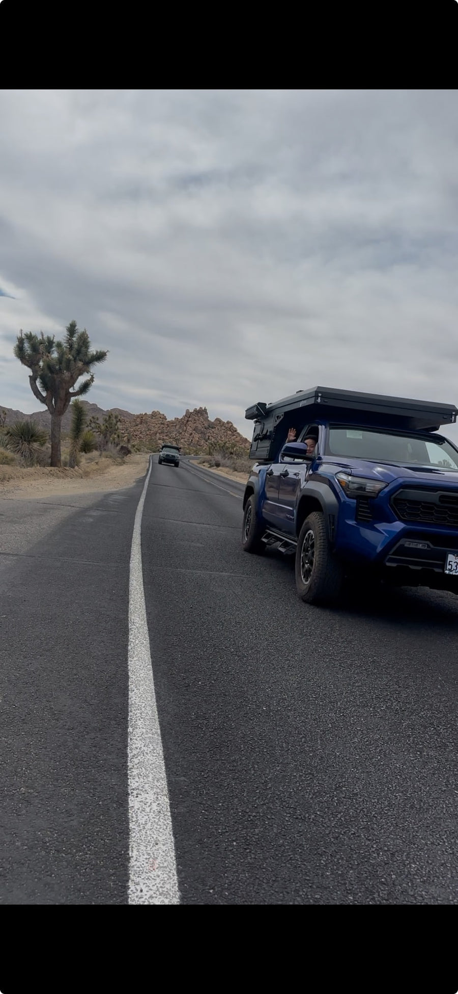A blue truck with a rooftop camper drives on a desert road