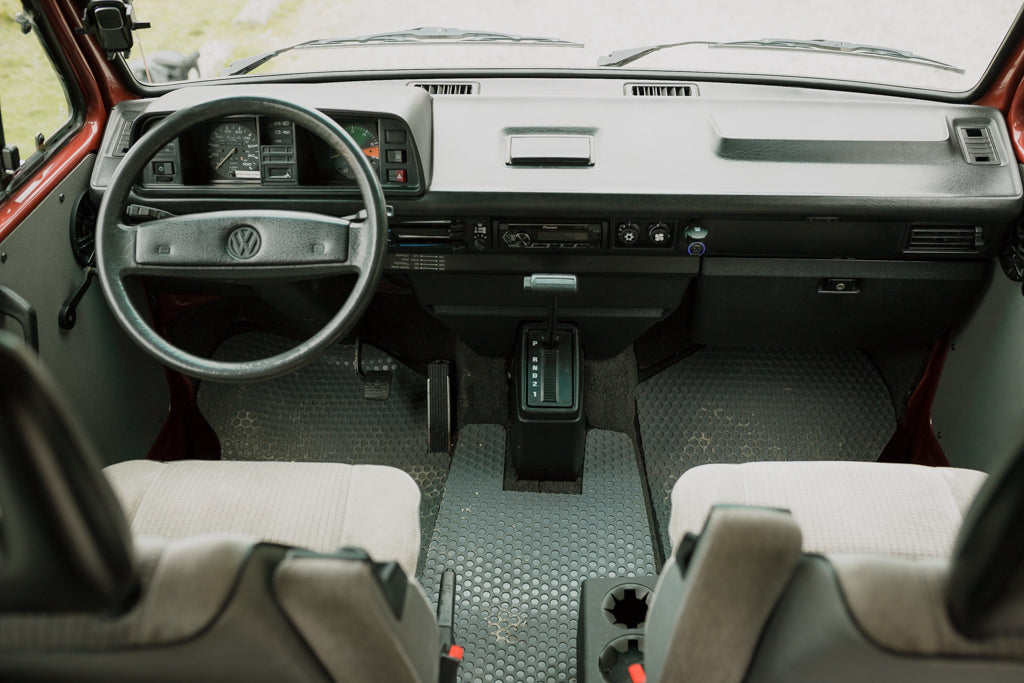 Front view of a vintage VW RV rental interior: dashboard, steering wheel, and gear shift visible. Ready for adventure.
