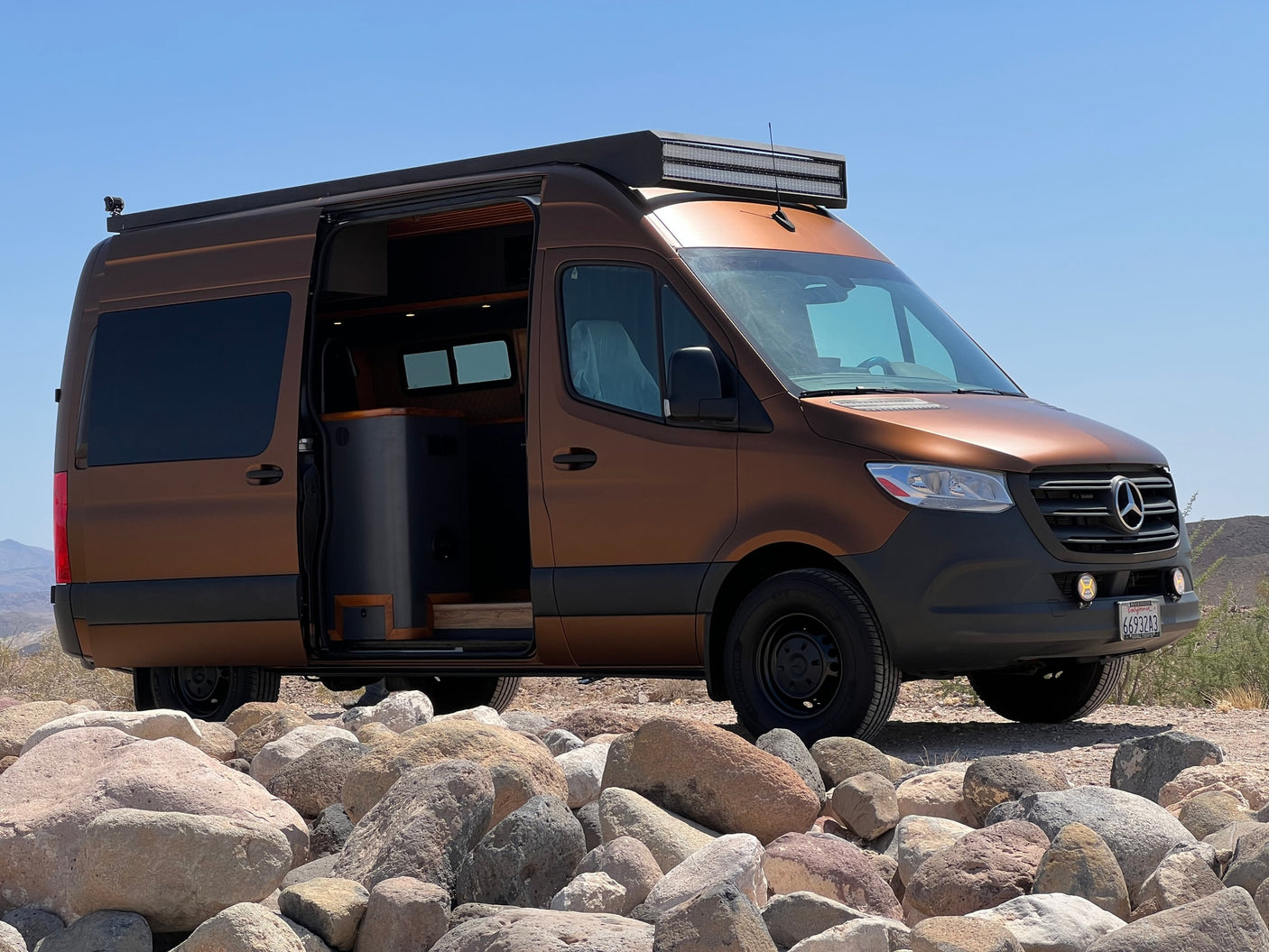 Stylish brown Mercedes-Benz Sprinter RV rental on rocky terrain under a clear sky