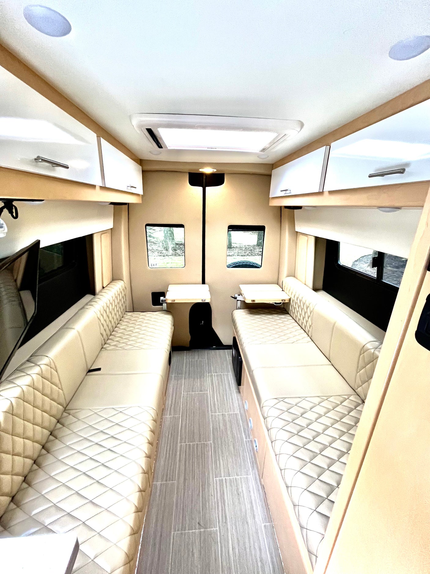 Clean, modern RV rental interior featuring plush, quilted bench seating, wood-look floor, and bright lighting.