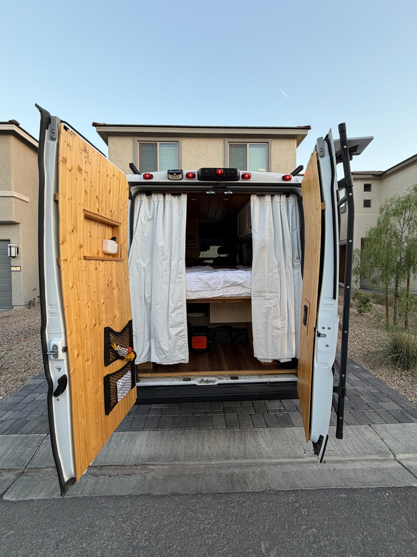 Custom rv rental interior visible through open rear doors, featuring a cozy bed, wood paneling, and practical storage for travel.