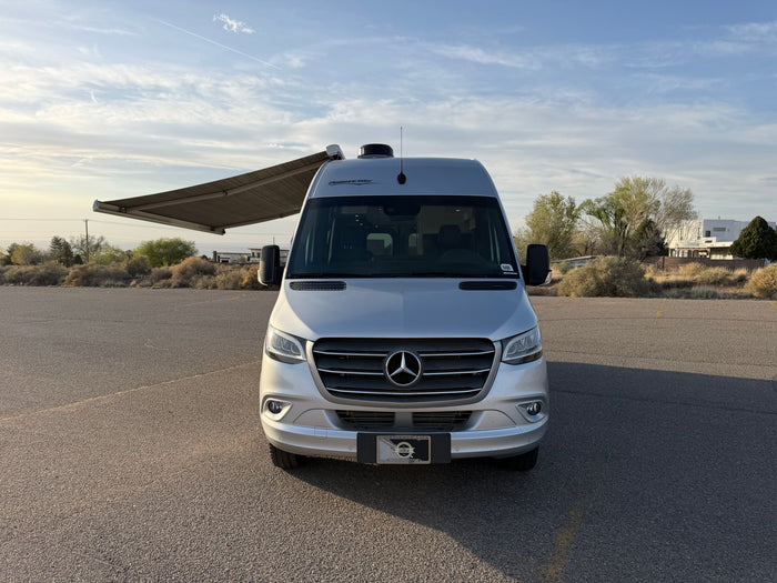 Pleasure-Way Mercedes-Benz Sprinter rv rental with awning extended, parked on asphalt, ready for travel.