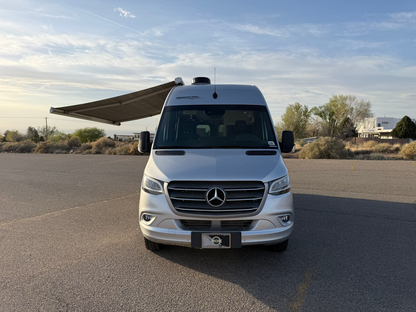 Pleasure-Way Mercedes-Benz Sprinter rv rental with awning extended, parked on asphalt, ready for travel.