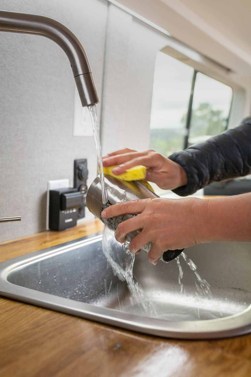 Enjoy modern amenities like a functional sink in your RV rental. Hands washing a metal cup under running water.