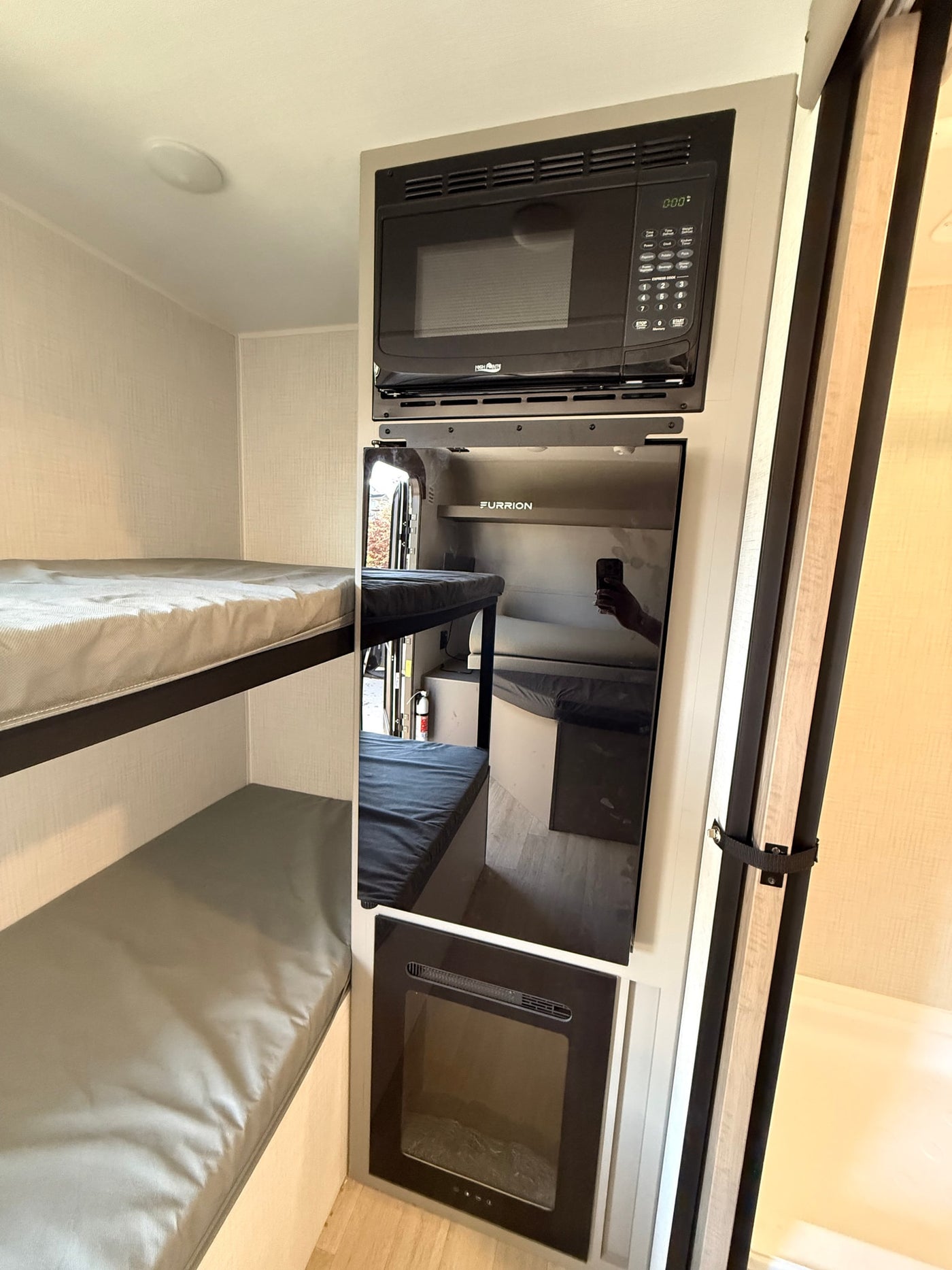 RV rental interior with compact bunk beds, a microwave, Furrion refrigerator, and electric fireplace for cozy travel. — photo 7