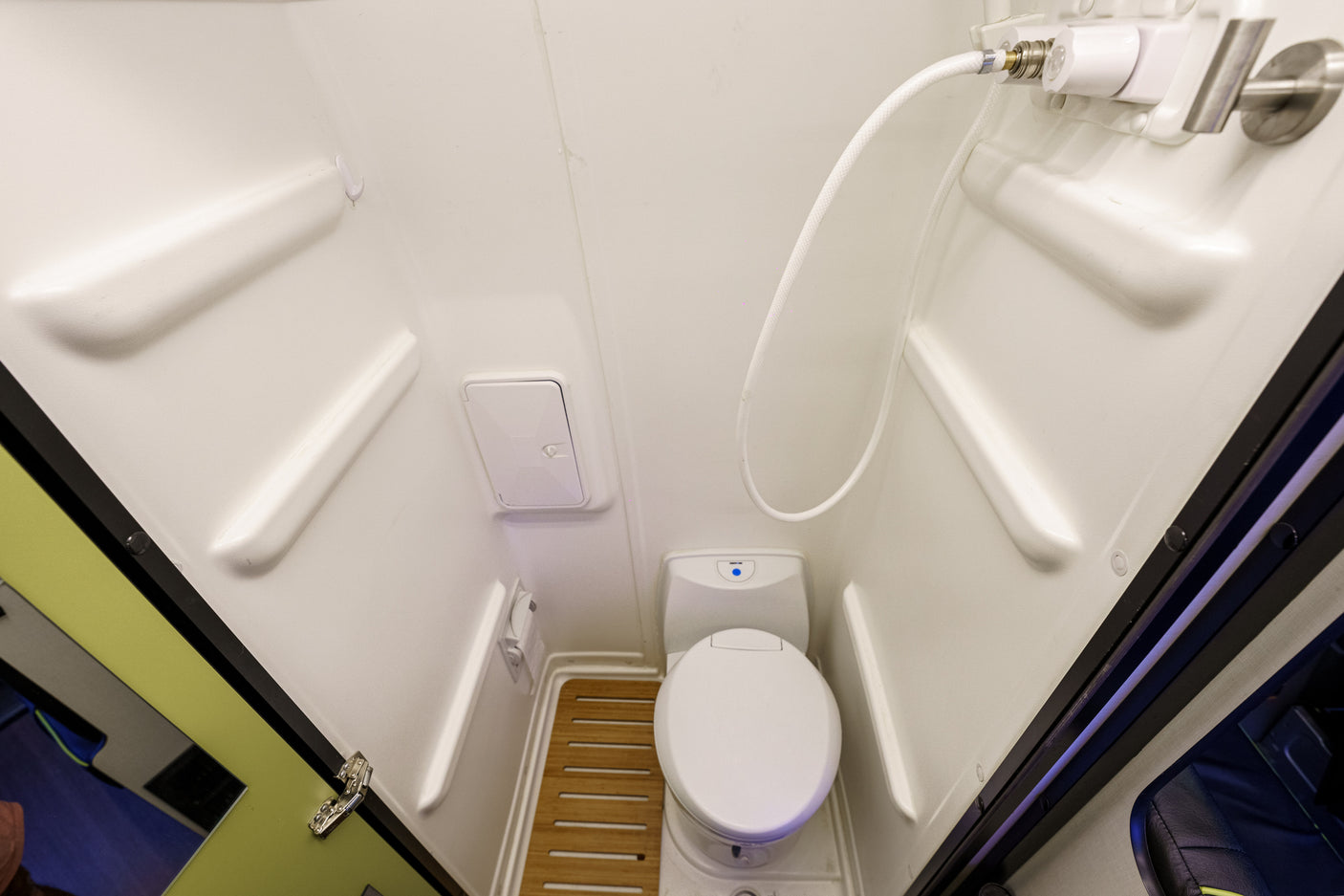 Compact white bathroom of an RV rental, featuring a toilet, shower, and wooden floor mat.