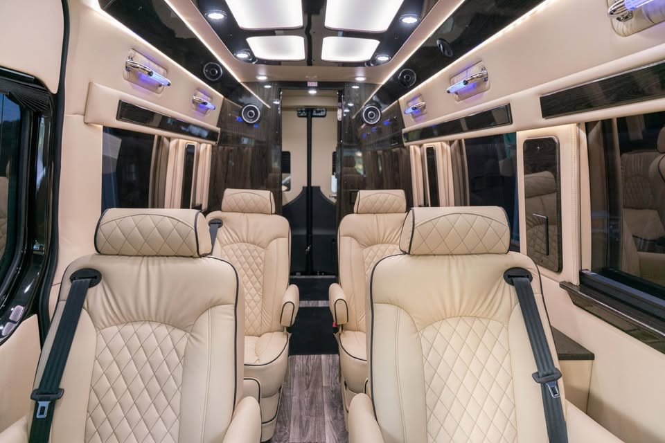 parked on a gravel path amidst lush green trees and a fence.|Spacious and luxurious RV rental interior: cream quilted leather seats