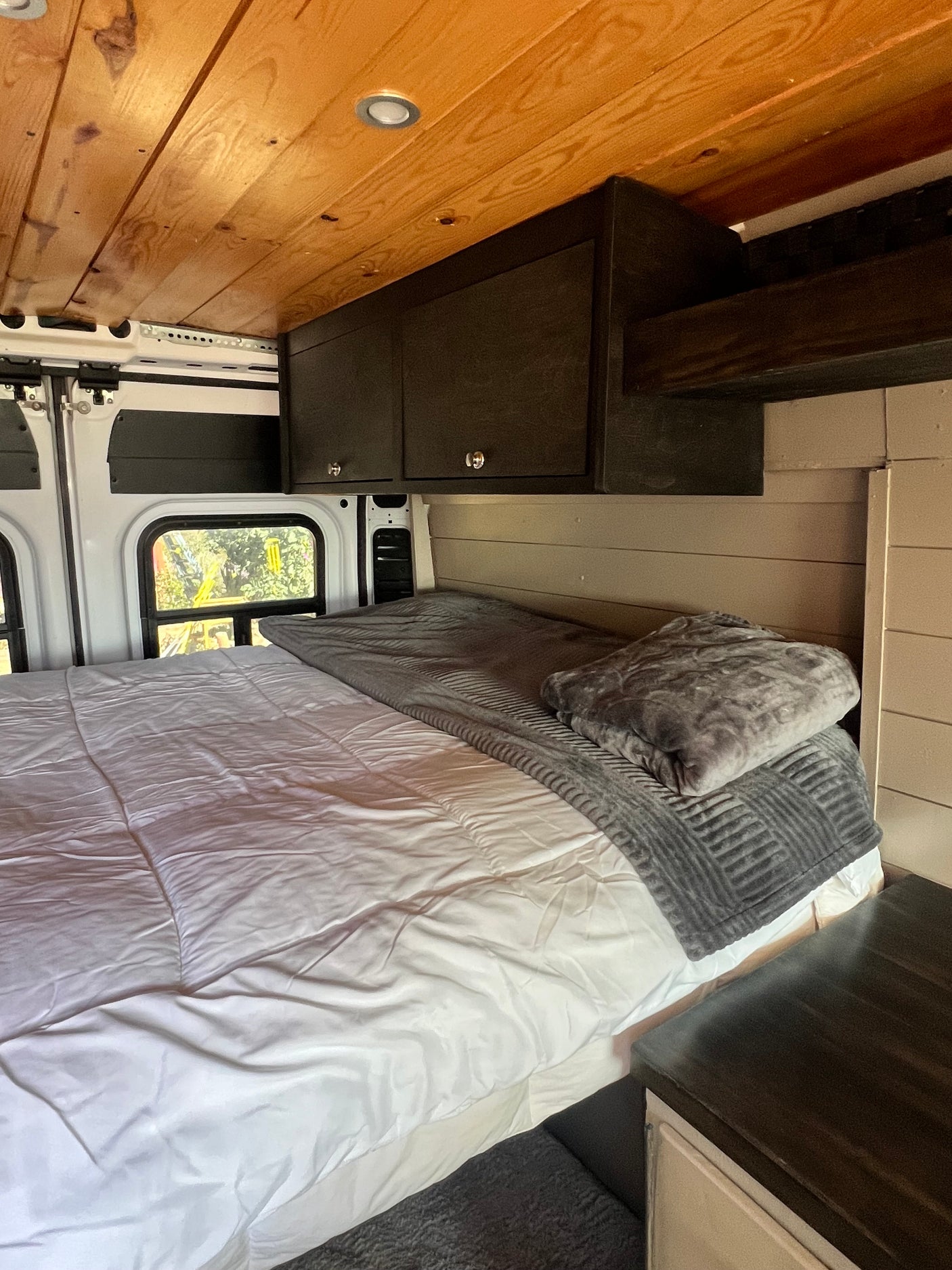 This RV rental features a cozy bedroom with a wooden ceiling, comfy bed, storage, and natural light from a window.