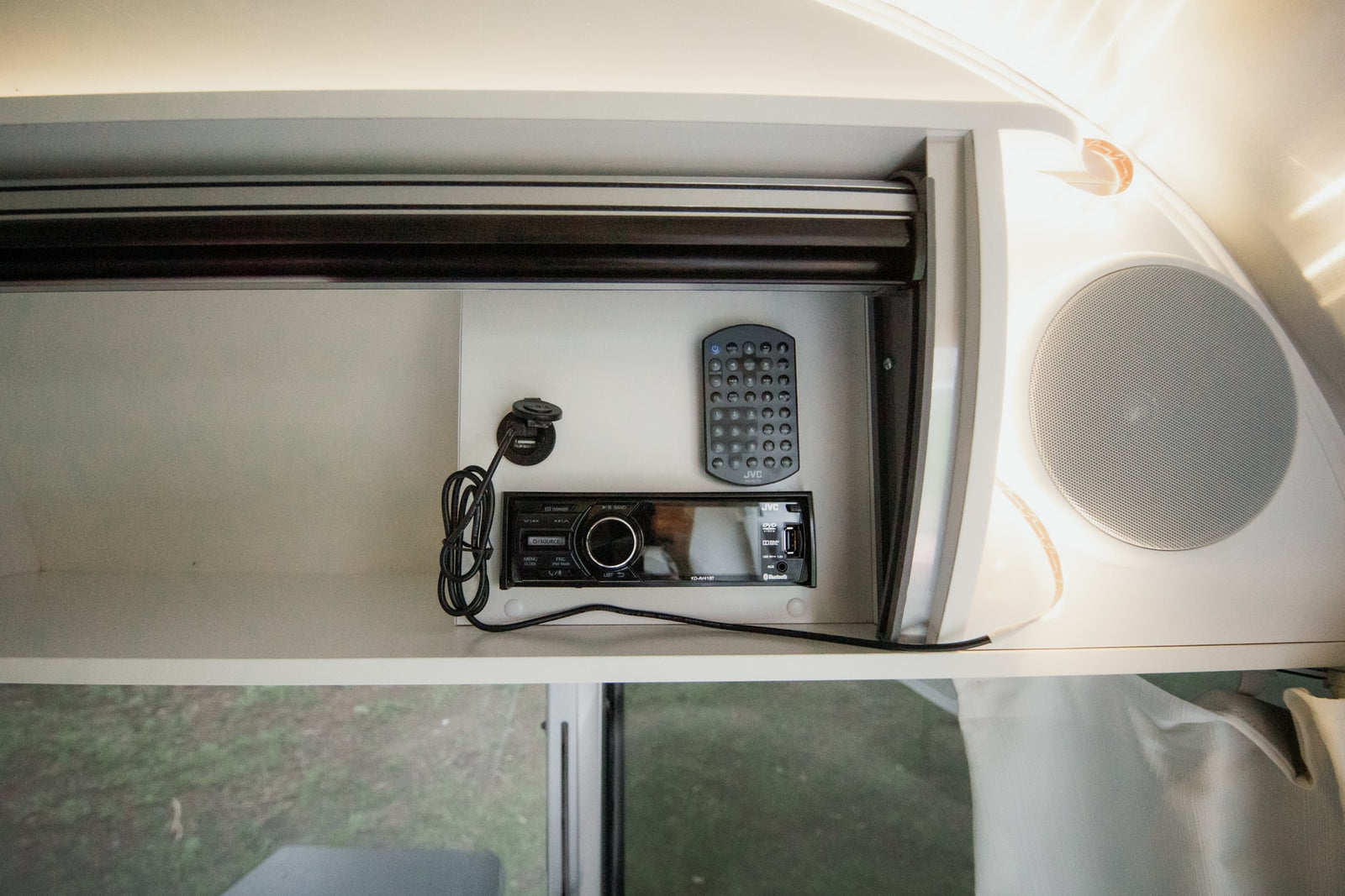 RV rental entertainment system featuring a JVC stereo, remote control, USB port, and speaker in an overhead compartment.
