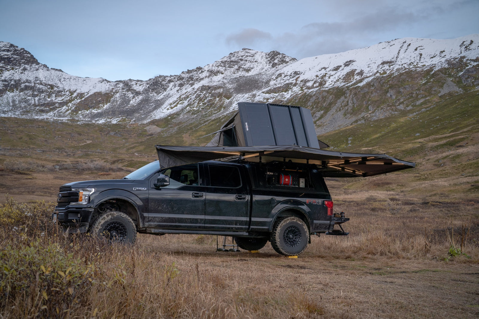 Overland F-150 with rooftop tent & awning deployed in mountains. Explore unique landscapes like this with an adventure RV rental!
