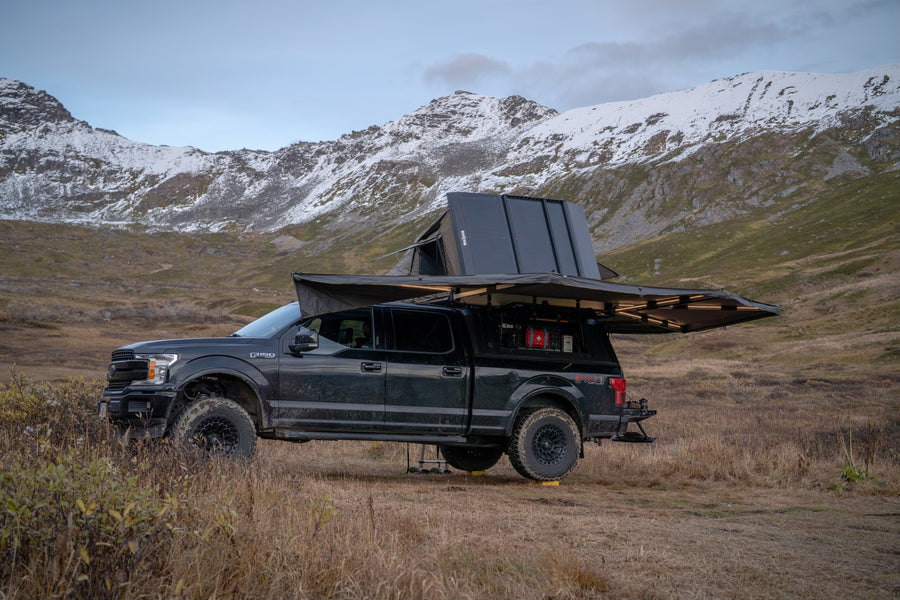 Overland F-150 with rooftop tent & awning deployed in mountains. Explore unique landscapes like this with an adventure RV rental!