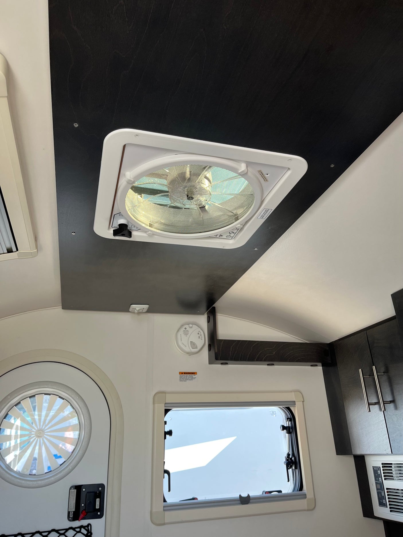 View inside an RV rental with ceiling fan, round window, rectangular window, smoke detector, and kitchen cabinets.