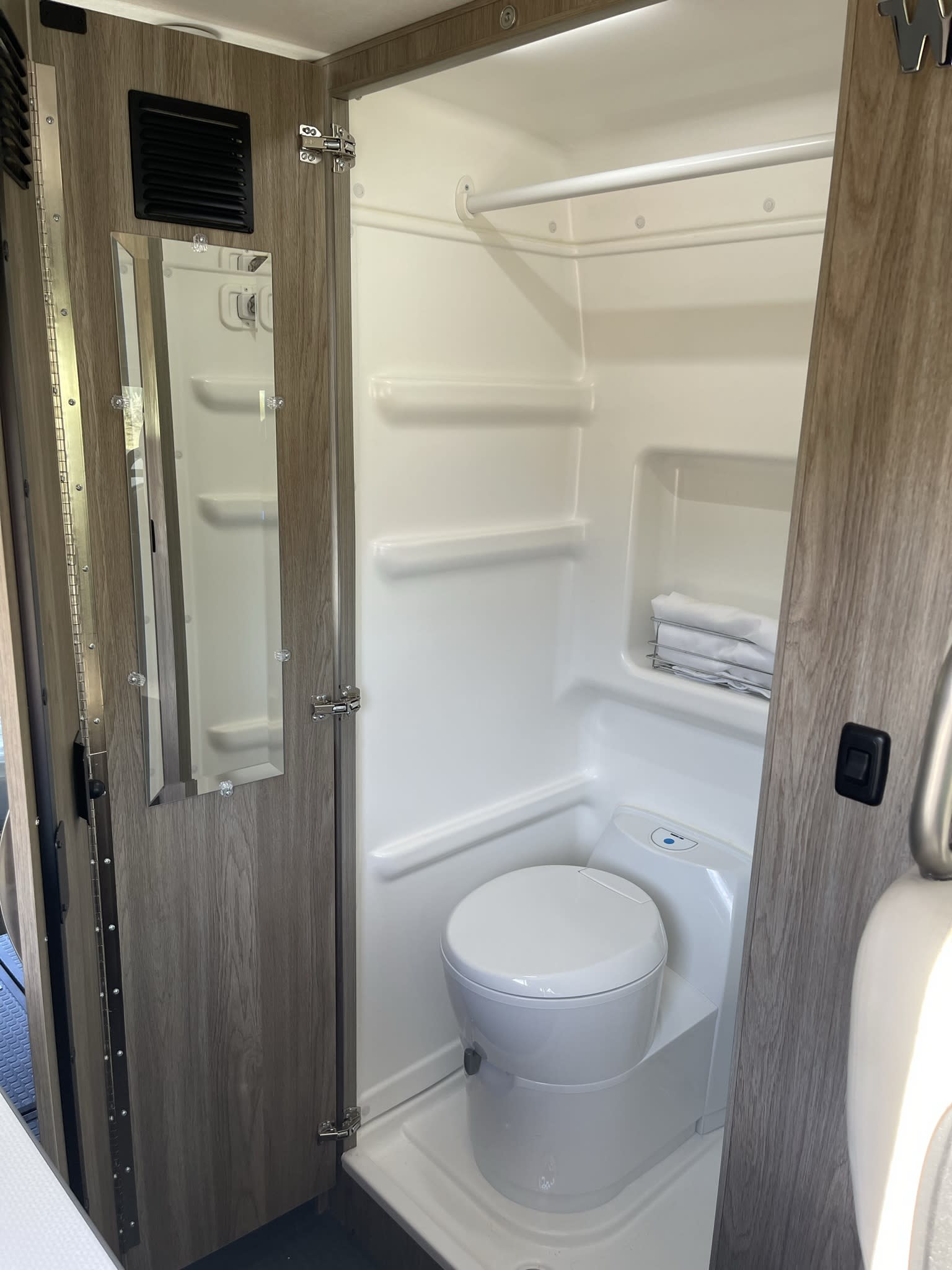 Compact RV rental wet bath featuring a toilet, shower, and a mirrored door with ventilation for practical travel comfort.