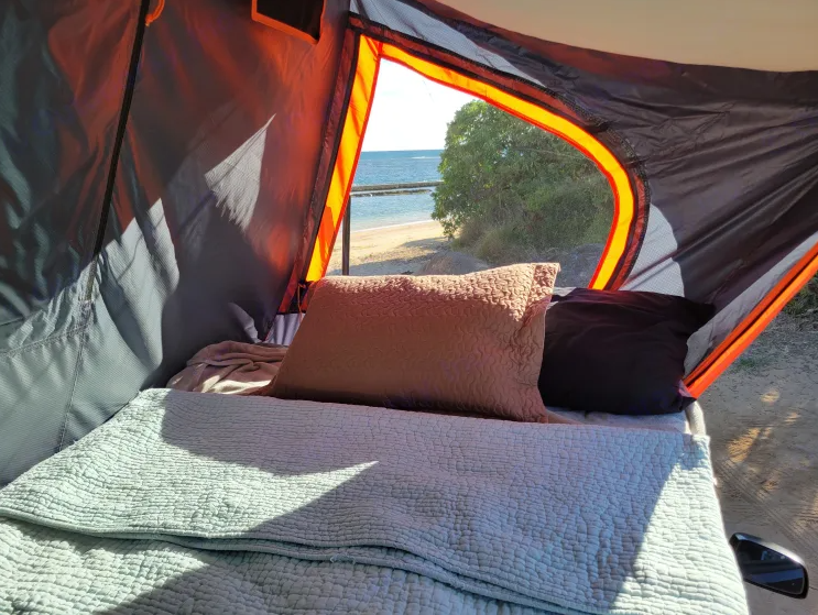 Cozy RV rental camping with a beautiful ocean view from inside the tent, featuring a comfortable bed.