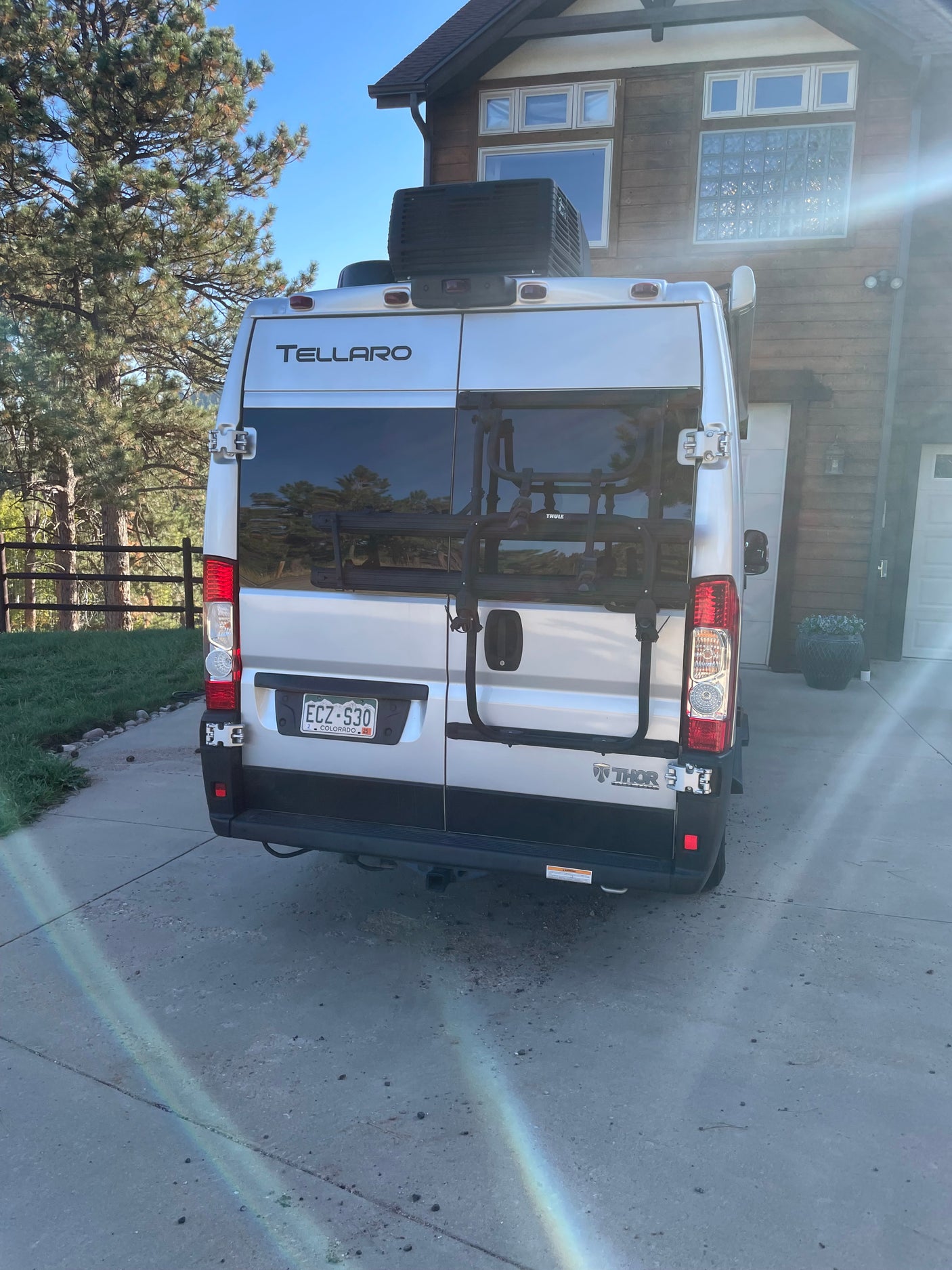 Silver Thor Tellaro RV rental with bike rack parked in a sunny driveway outside a house.