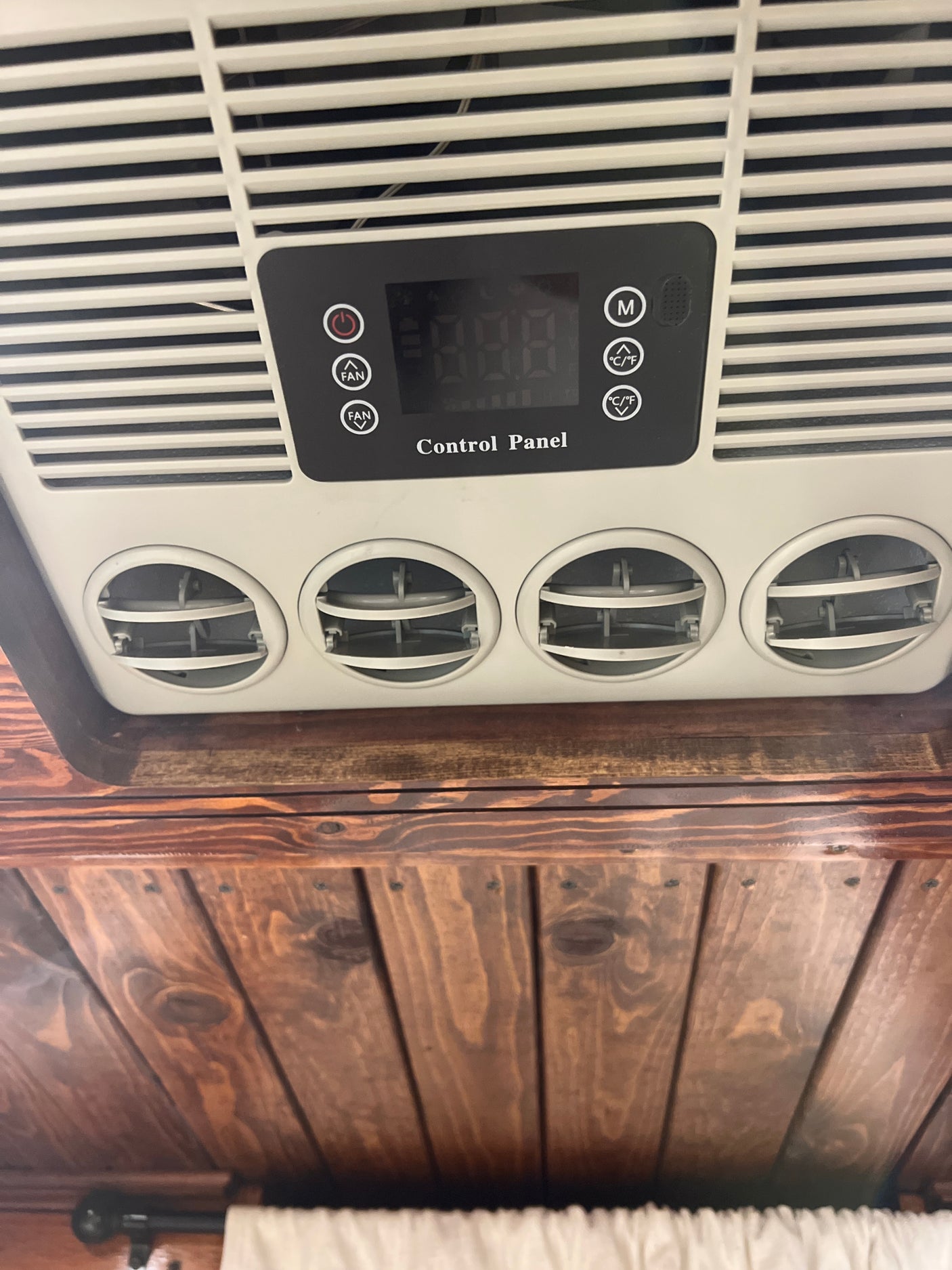 Overhead RV rental AC unit with a digital control panel, adjustable fan settings, and four circular air vents on a wooden ceiling.
