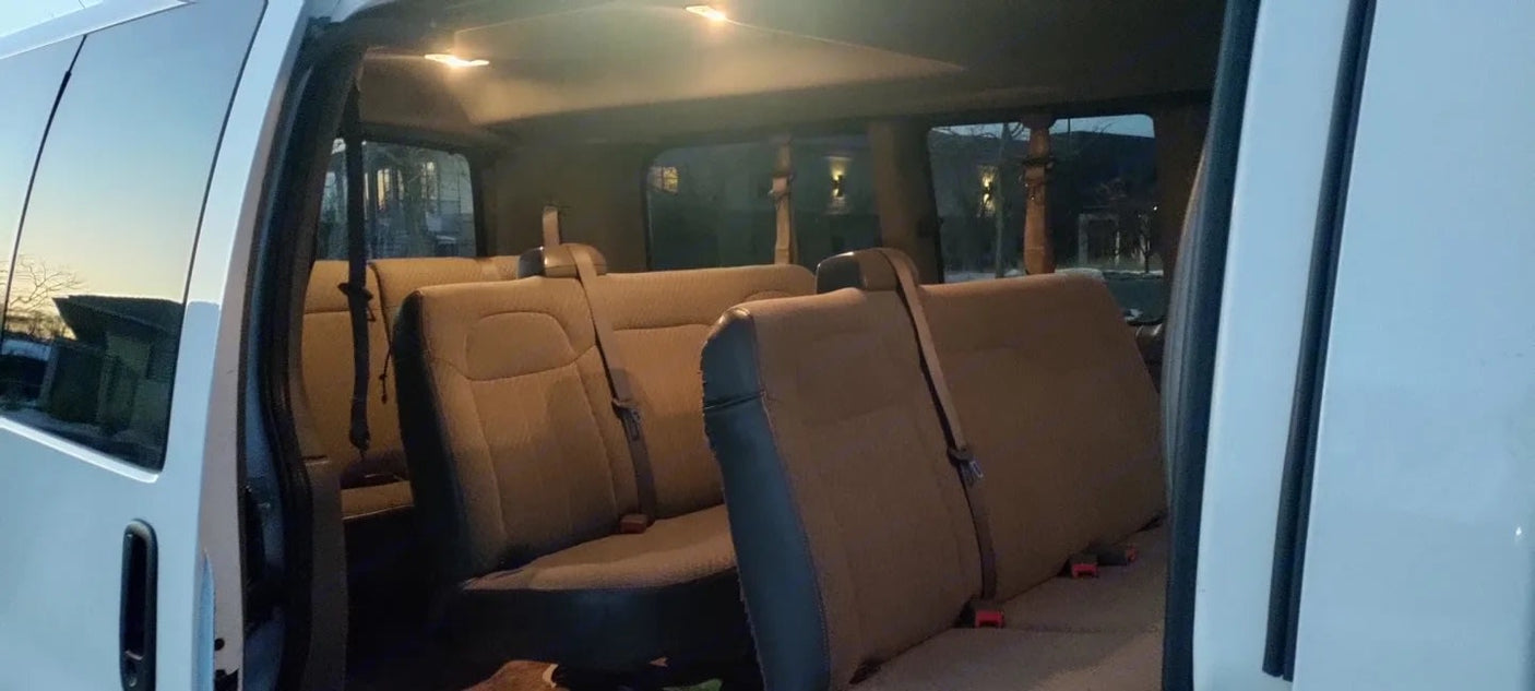 RV rental: Inside a well-lit passenger van showing multiple rows of beige seating and overhead lights.