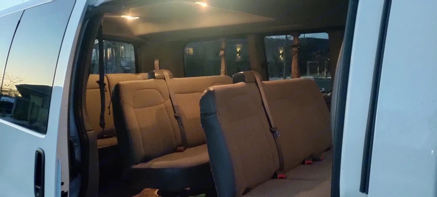 RV rental: Inside a well-lit passenger van showing multiple rows of beige seating and overhead lights.