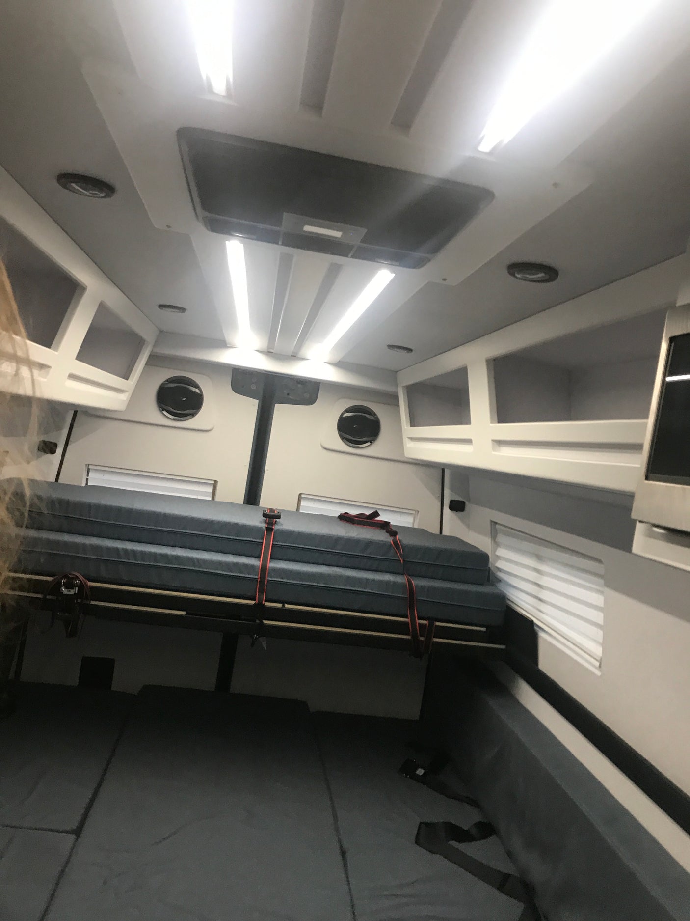 Inside an RV rental, a compact sleeping area with a secure bunk bed, lower mattress, bright lights, and cabinets for efficient travel.